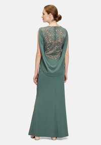 Langes grünes Kleid mit einem Spitzenrücken-Design. Weicher, fallender Stoff, ärmellos mit einem bodenlangen Schnitt und einer glatten Textur.