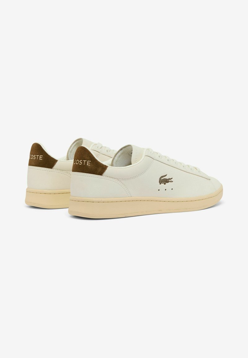 Sneakers basse bianche con suole beige, linguette in camoscio marrone sul tallone e un piccolo logo del coccodrillo sul lato e "Lacoste" sul tallone.