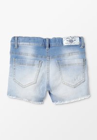 Pantalones cortos de denim decolorido en azul claro con dobladillos deshilachados, dos bolsillos traseros y una etiqueta de parche blanca en la cintura.