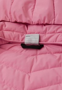 Wnętrze różowej kurtki puchowej o pikowanej fakturze. Zawiera metkę z informacjami o pielęgnacji z czarną etykietą. Miły w dotyku materiał, podkreślający ciepło i komfort.