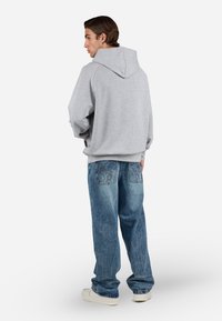 Grå hættetrøje med løs pasform, parret med udvaskede blå jeans med broderede baglommer og hvide sneakers.