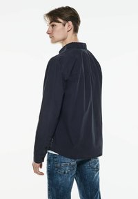 Mörkblå långärmad skjorta med krage som knäpps, mjuk textur och svängd sidsöm. Kombinerad med texturerade blå denimjeans.