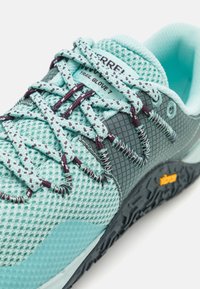 Světle modrá síťovina běžecké boty na trail s tmavě šedými akcenty, texturovaná podešev, pletené tkaničky ve světle modré a tmavě fialové a logo Vibram.