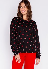 Svart långärmad sweatshirt med spridd läpptryck i röd och rosa. Har randiga muddar och en avslappnad passform. Tillsammans med röda ribbade byxor.