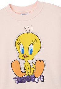 Lichtroze sweatshirt met een cartoonvogelafbeelding met blauwe ogen, omringd door rhinestones, en "TWEETY" in paarse sequins.