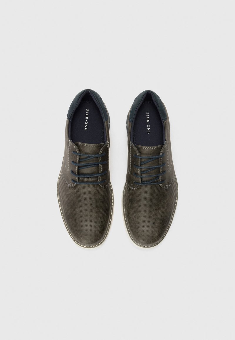 Zapatos de cuero perforado oscuro con detalles en azul marino, diseño con cordones y costuras blancas contrastantes a lo largo de la suela. Perfil plano con acabado texturizado.