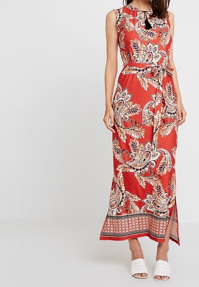 Abito maxi rosso senza maniche con un intricato motivo paisley, colletto a strati, vita con cintura e una fessura laterale all'orlo.