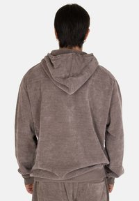 Felpa in corduroy marrone foderata in pile, con cappuccio regolabile, polsini a costine e vestibilità comoda. Tessuto testurizzato con una leggera lucentezza.