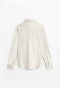 Camicia in seta di colore crema chiaro, con colletto classico, maniche lunghe e orlo curvato. Tessuto liscio con dettagli ai polsini.