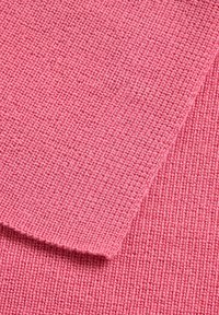 Geribbelde, zachte stof in een lichtroze kleur, met een textuur en fijne, gelijkmatige stiksels. Twee overlappende stukjes stof zijn zichtbaar.