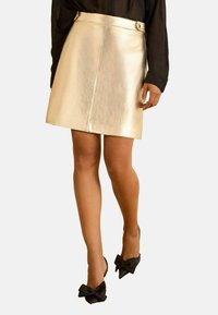 Sieviete tērpusies zelta metāliska mini svārkā ar asimetrisku priekšpusi un melnus, ar lielām lokām rotātus, smailus papēžus.