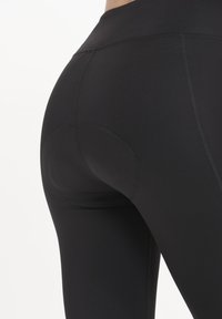 Black high-waisted leggings made of smooth, stretchy fabric. Features flatlock seams and a curved panel design on the rear.