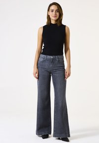 Zwarte geribbelde mouwloze top gecombineerd met hoge taille, wijde grijze denim jeans. Accentueert met een frontknop en riemlussen.