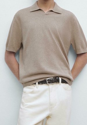 Person wearing a beige short-sleeve knit polo shirt tucked into off-white pants with a woven dark brown belt.