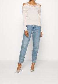 Jasnoróżowy sweter z odsłoniętymi ramionami i koronkowymi detalami, zestawiony z jasnoniebieskimi wysokim stanem jeansami oraz srebrnymi szpilkami z ostrym noskiem.