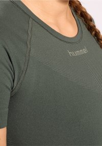 Mörkgrön, kortärmad sporttröja med ribbad struktur, figurnära design och logotyp på bröstet. Sömmar längs axlar och halsringning.