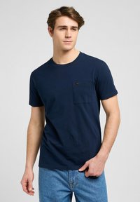 Granatowa bawełniana koszulka z krótkim rękawem, okrągłym dekoltem i kieszonką na piersi. Posiada małą metkę wszytą w kieszeń.