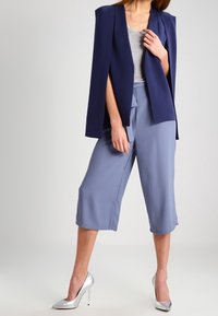 Blazer blu navy con spalle strutturate, top grigio e culotte azzurro chiaro. Tacchi alti argento completano l'outfit con una texture liscia.