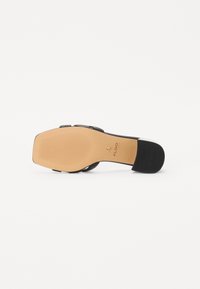 Schwarze Sandale mit Absatz und einer glatten, strukturierten Sohle. Das design mit Riemchen weist eine elegante Silhouette auf. Logo ist auf der Innensohle geprägt.