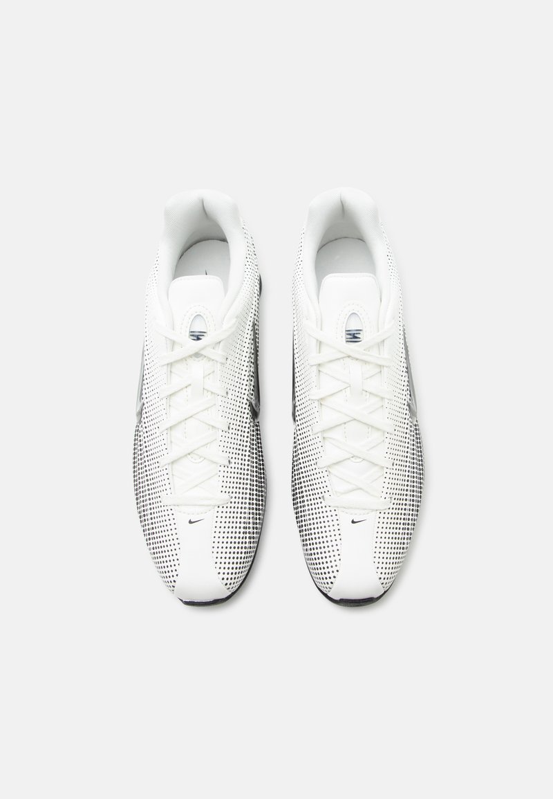 Par de zapatos deportivos blancos con patrón de puntos negros, cordones blancos y pequeño logo negro de swoosh, vistos desde arriba sobre un fondo claro.