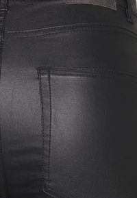 Zwarte faux leren broek met stikdetails, een zijzak en een gladde textuur. De stof heeft een glanzende afwerking.