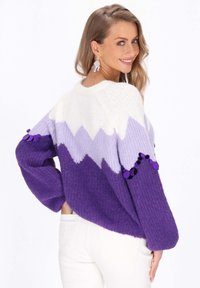 Pulover tricotat violet cu model gradient în zigzag, având secțiuni albe și lavandă, decorat cu accente de pom-pom pe mâneci.