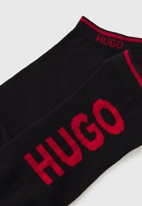 Schwarze Socken aus weichem Material mit einem auffälligen roten "HUGO"-Logo an den Seiten und einem kontrastierenden roten gerippten oberen Rand.