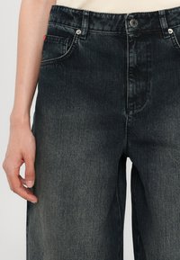 Jeans in denim scuro con vita alta, caratterizzati da un design a cinque tasche, leggero sbiadimento e chiusura con bottone. Il materiale ha una texture liscia.