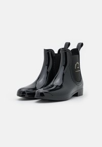 Botas Chelsea de goma negras y brillantes con paneles laterales elásticos y lengüetas para poner y quitar fácilmente. Diseño de tacón bajo y punta redondeada.