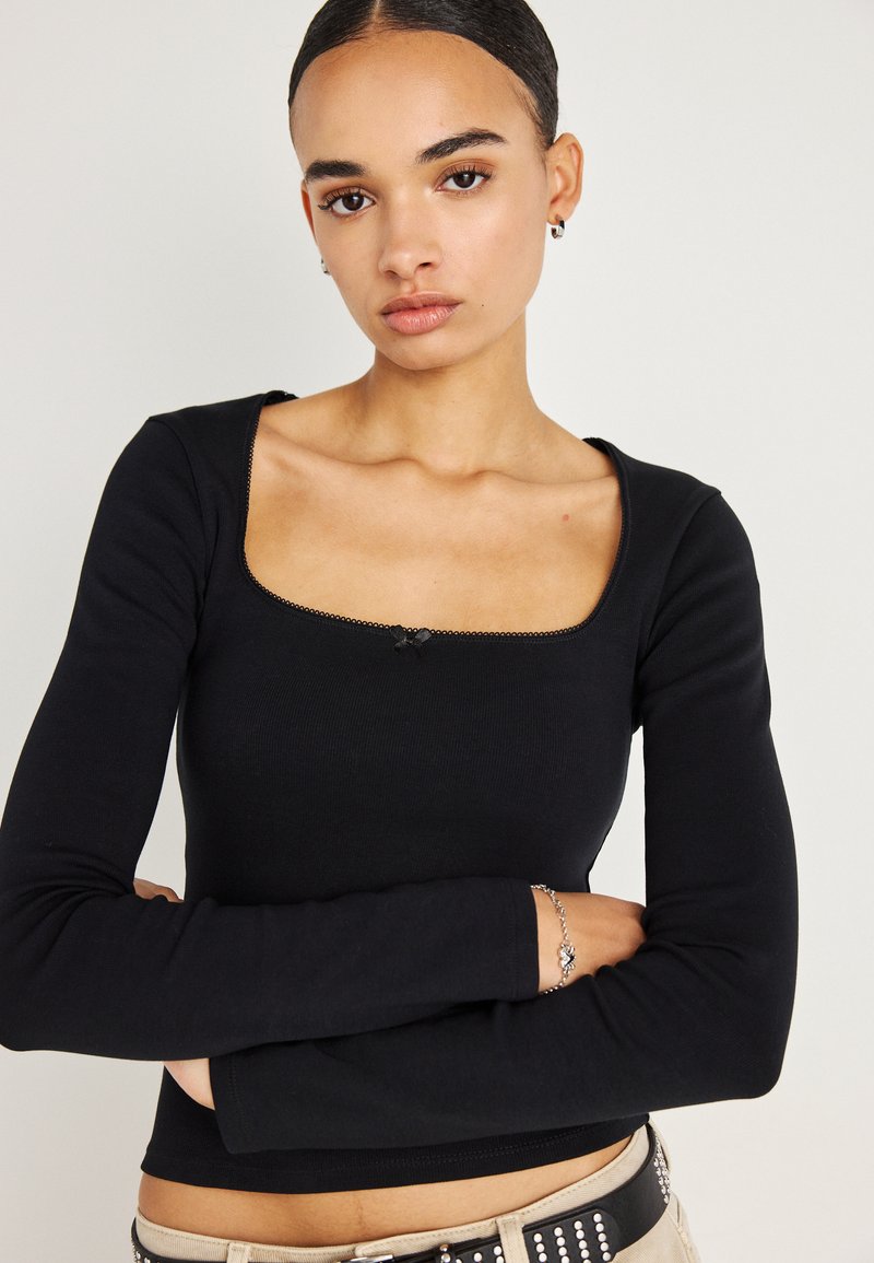 Juoda ilgarankovė palaidinė su kvadratiniu iškirpimu, ribuota tekstūra ir dekoratyvine maža skarele centre. Paprastas ir prigludęs dizainas.