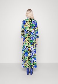 Mekko, jossa on eloisa kukkakuvio sinisellä, keltaisella ja vihreällä mustalla taustalla; siinä on kolmivartiset hihat ja rento istuvuus.