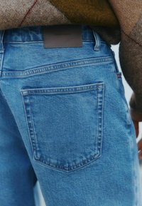 Jeans in denim azzurro chiaro con un design delle tasche semplice e un'etichetta in pelle marrone con la scritta "DENIM SUPPLY" sulla vita.