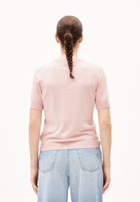 Pink short-sleeve sweater with ribbed cuffs and hem, worn with high-waisted light blue jeans. Model's hair is styled in a braid.