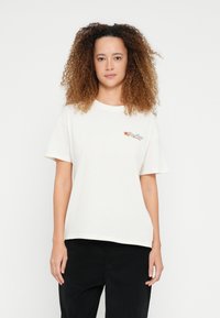 Tričko barvy smetany vyrobené z měkké bavlny. Má krátké rukávy a kulatý výstřih, s květinovou výšivkou na hrudi.