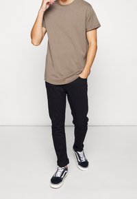 T-shirt marron à manches courtes, design uni, col rond. Pantalons noirs ajustés avec poches latérales. Baskets noires et blanches avec lacets.