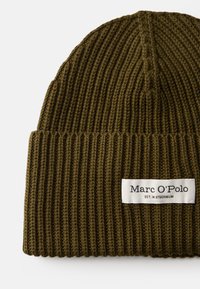 Olivi vihreä ribbien neulepipo, jossa on käännetty reuna ja valkoinen label, jossa lukee "Marc O'Polo EST. IN STOCKHOLM." Pehmeä rakenne ja yksinkertainen muotoilu.