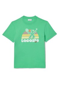 Camiseta de algodón verde con un estampado gráfico de un jugador de tenis y la palabra "Lacoste" en blanco, sobre un fondo de rayas multicolores.