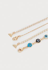 Chaîne superposée dorée avec des charms en forme de triangle et ronde, ornés de détails bleus et noirs, finition lisse et fermoirs à pince récursive.