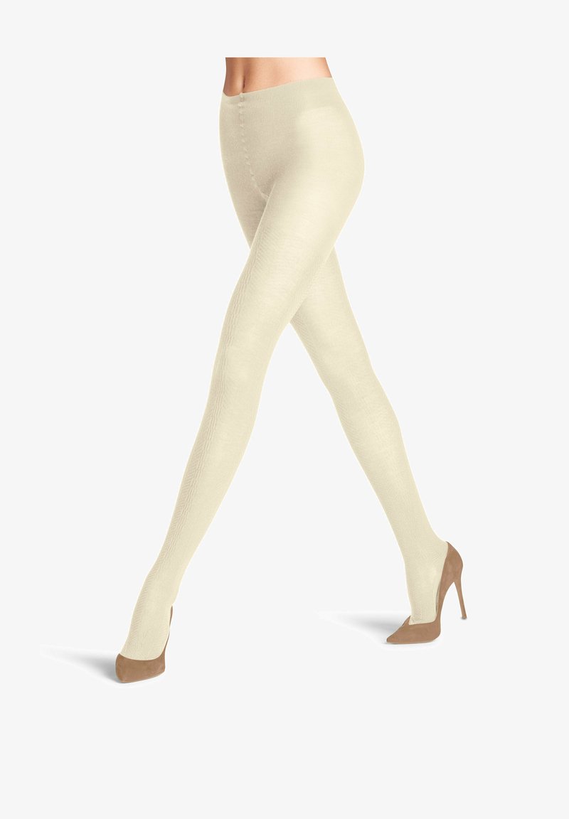 Collant crema con trama e finitura liscia, caratterizzati da un alto talle e un design aderente, abbinati a scarpe con tacco nude.