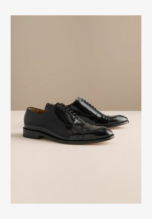Czarne lakierowane pantofle z zaokrąglonym noskiem, zapinane na sznurowadła, z niewielkim obcasem i subtelnym przeszyciem wzdłuż szwów.