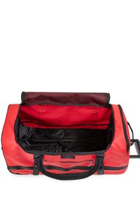 Red duffel bag with black accents, made of durable material. Features a wide opening, interior straps, and a mesh pocket. Spacious design.