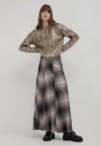 Pull en métal doré texturé avec un motif en vagues, associé à une longue jupe à carreaux dans des tons de rose, gris et noir ; chaussures noires.