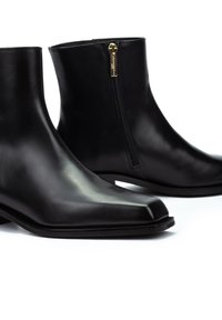 Botines de cuero negro con un diseño elegante. Cuentan con una puntera puntiaguda y un cierre lateral con herrajes dorados. Textura suave y suela plana.