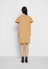 Robe en coton tan avec des manches courtes à volants, une coupe droite et un design de couture simple, associée à des bottines noires.