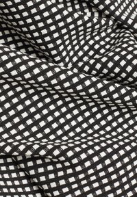 Tissu noir avec un motif en grille carrée blanche, montré en gros plan avec des plis et une texture visibles.