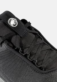 Svart atletisk sko med en texturerad tygöverdela, snörning och en rund logodesign med en elefant.