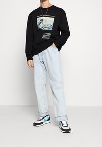 Sudadera negra con gráfico de ola, jeans azul claro y zapatillas negras con detalles en turquesa. Corte holgado, material suave.