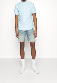 Svetle modrá košile s krátkým rukávem na knoflíky a límcem, spárovaná se světle modrými džíny, bílými ponožkami a bílými teniskami.