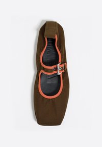 Zapato de tela marrón con acentos naranjas, diseño redondeado, correa ajustable con hebilla plateada y un interior negro suave.