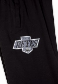 Zwarte katoenen joggers met een grijs en zwart 'Mud City REYES' logo met een kroon. Inclusief een taillebandzak voor extra gemak.